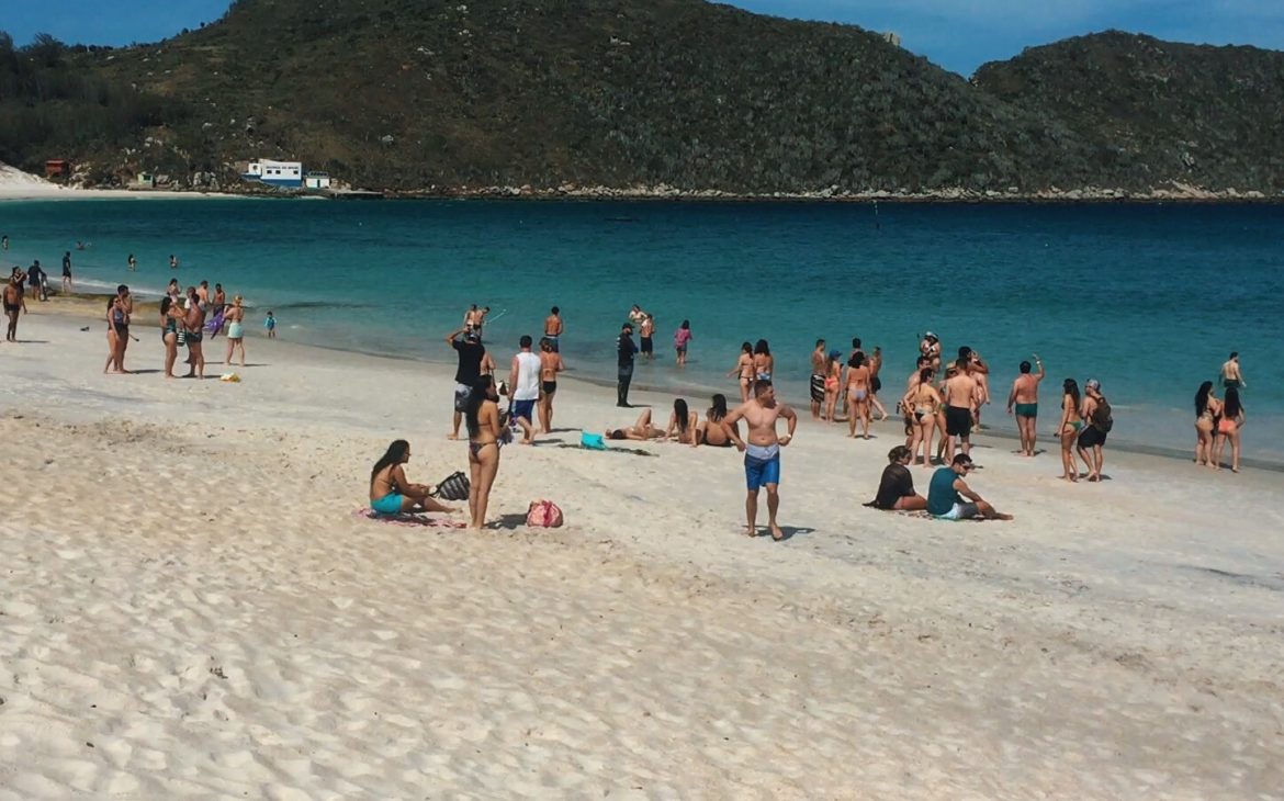 Turistas na areia de frente para o mar, curtindo o dia na Praia do Farol em Arraial do Cabo